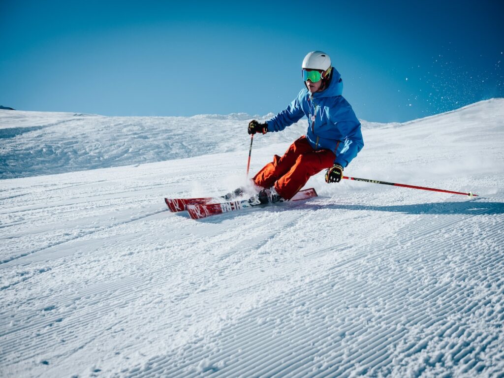 A skier going fast down the mountain with a blue jacket and orange pants.