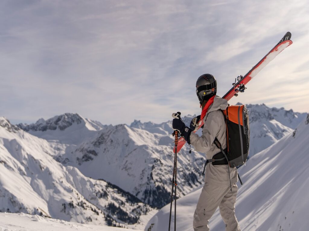 A man holding his skis at the western ski resort that does not allow snowboarding.