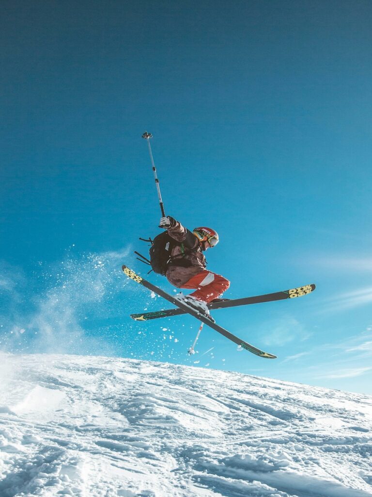 A skier jumping on a ski slope with blue skies in the distance.