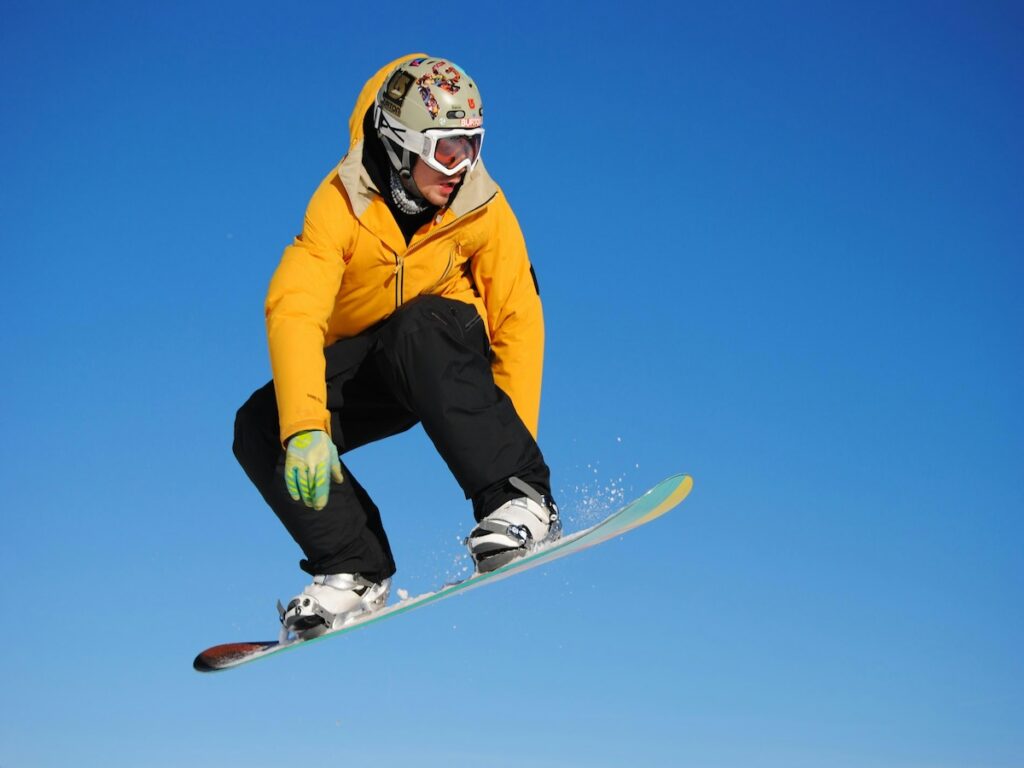 A snowboarder jumping with a yellow jacket and blue skies.