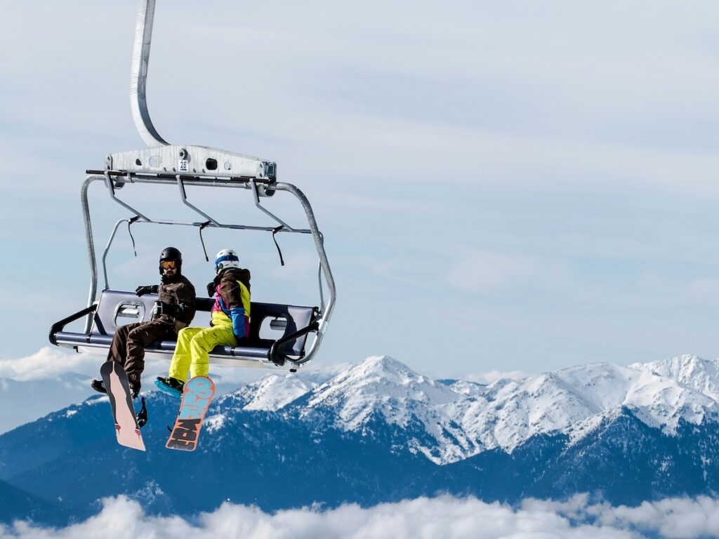 A skier and a snowboarder sitting on a lift with mountains in the distance.