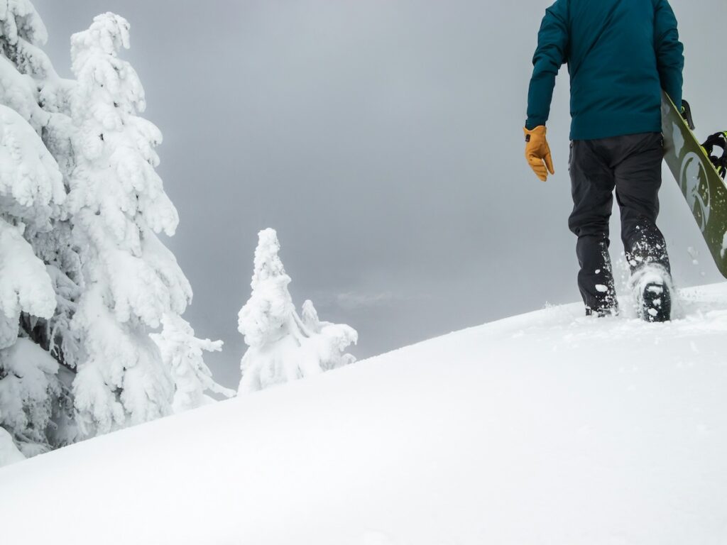 A snowboarder hiking up the mountain while carrying his green board.