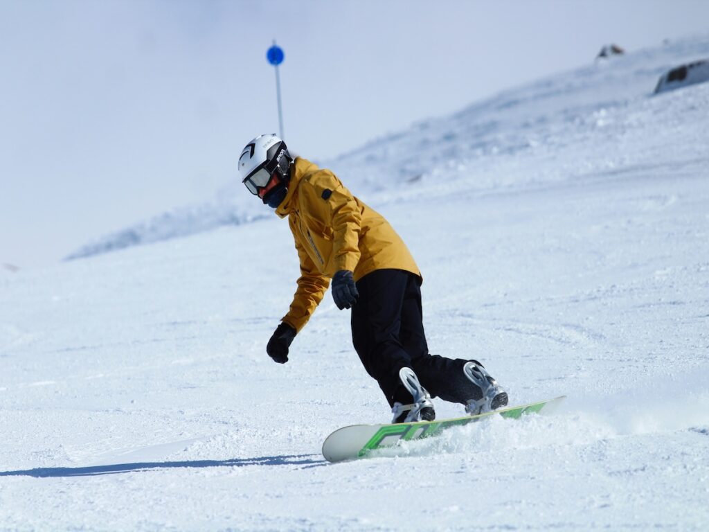 A snowboarder easily going down the slope in a yellow jacket.