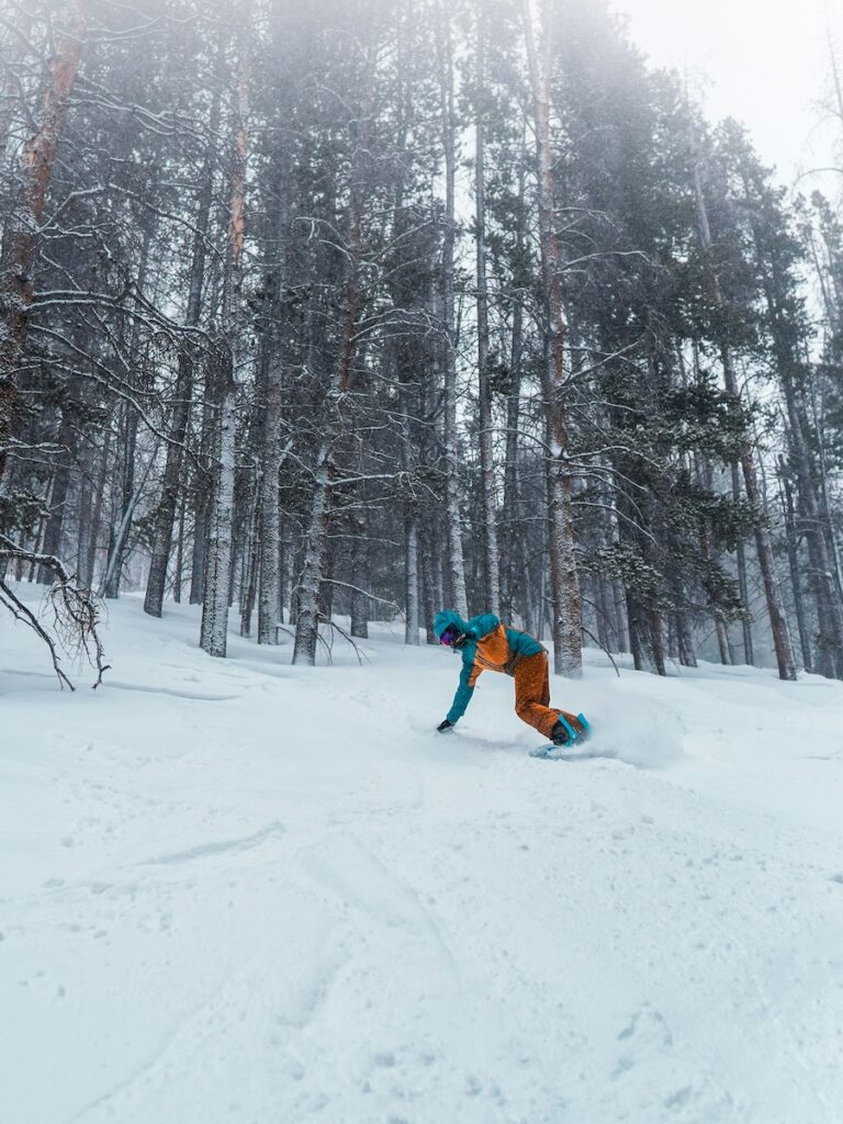 A snowboarder touching the snow coming out of the trees.