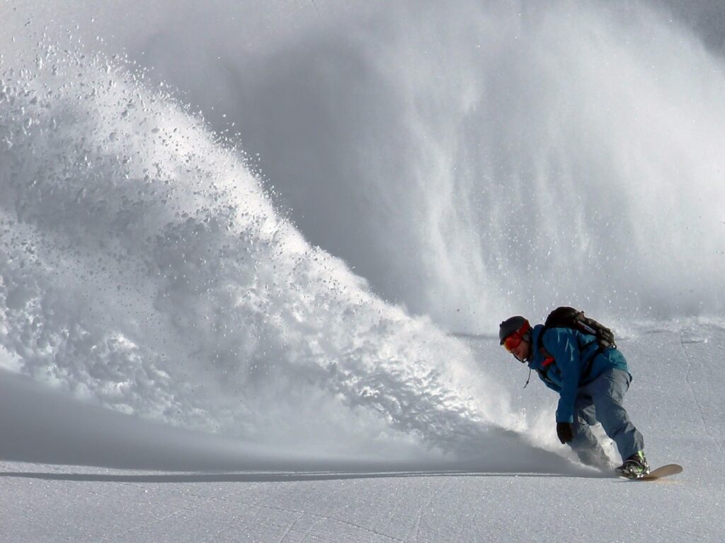 A snowboarder spraying snow on untouched powder.