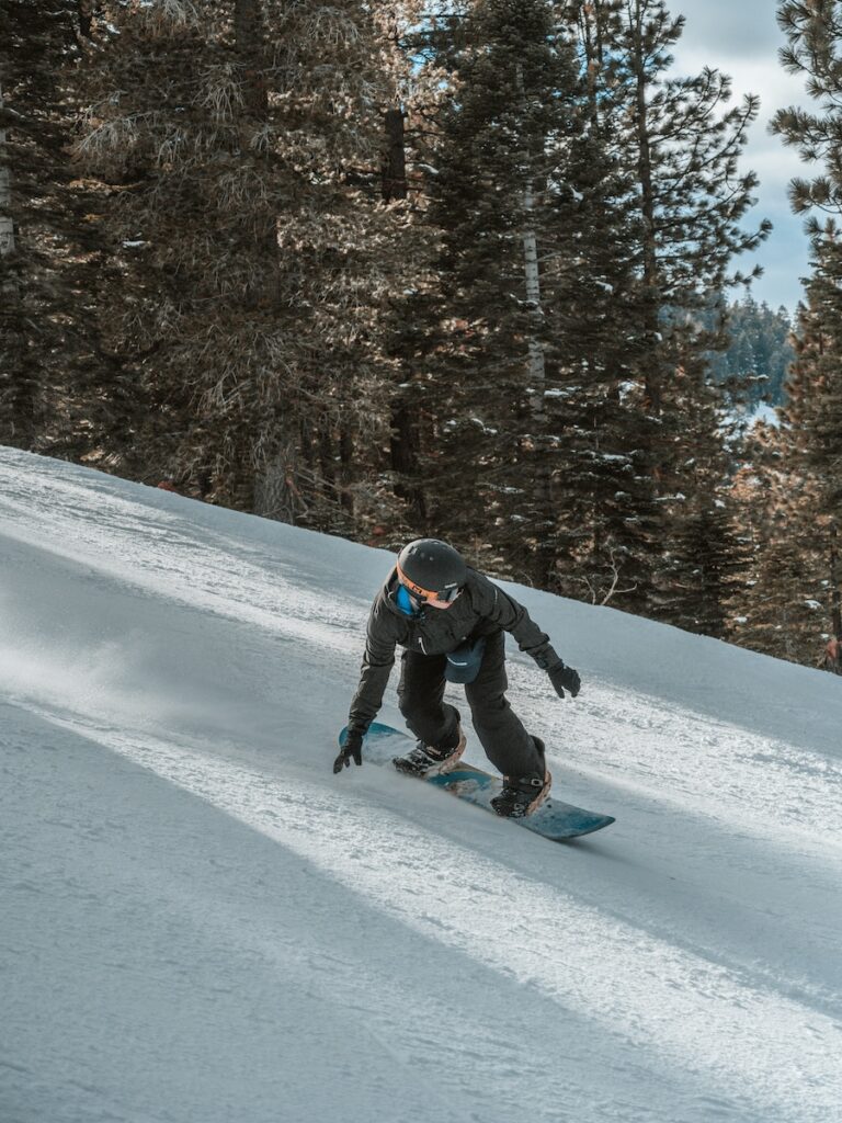 A snowboarder going down the mountain and leaning towards the slope.