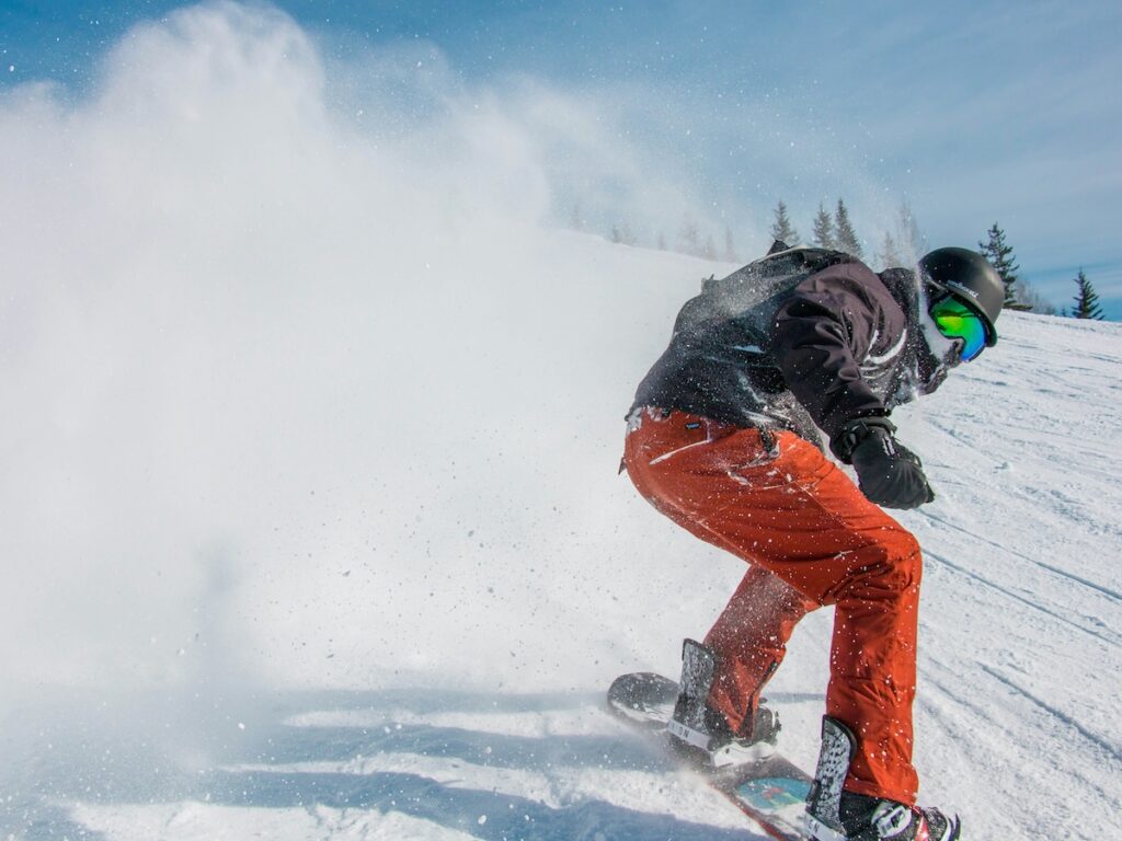 A snowboarder going fast down a ski slope with orange pants and a black jacket.