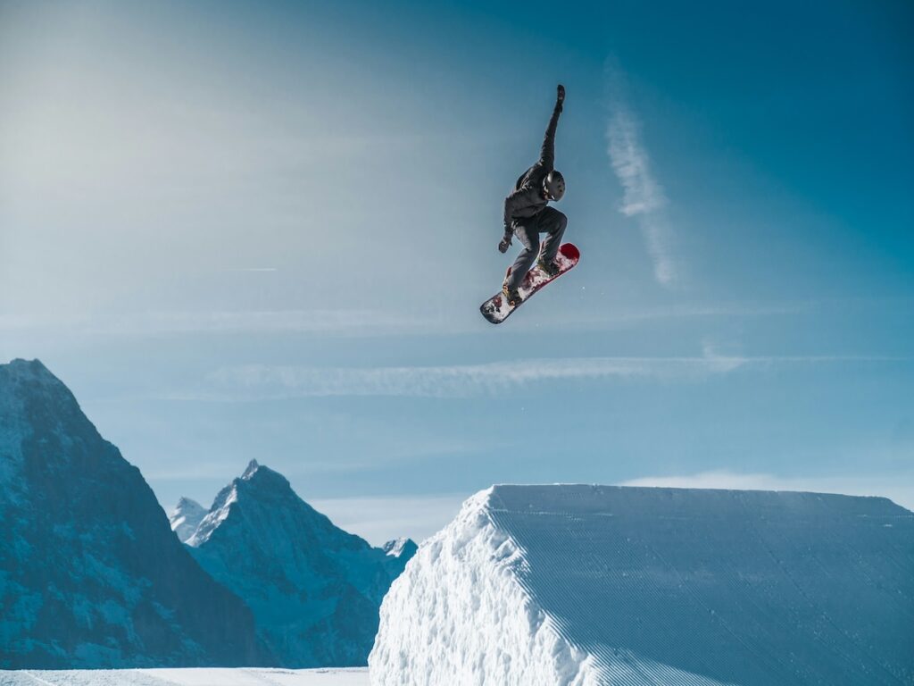 A snowboarder listening to some of the best snowboarding songs while jumping off a jump.