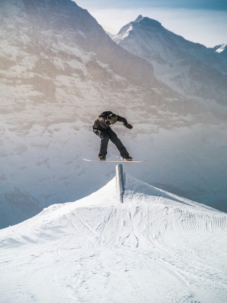 A snowboarder jumping on an obstacle with mountains in the distance.