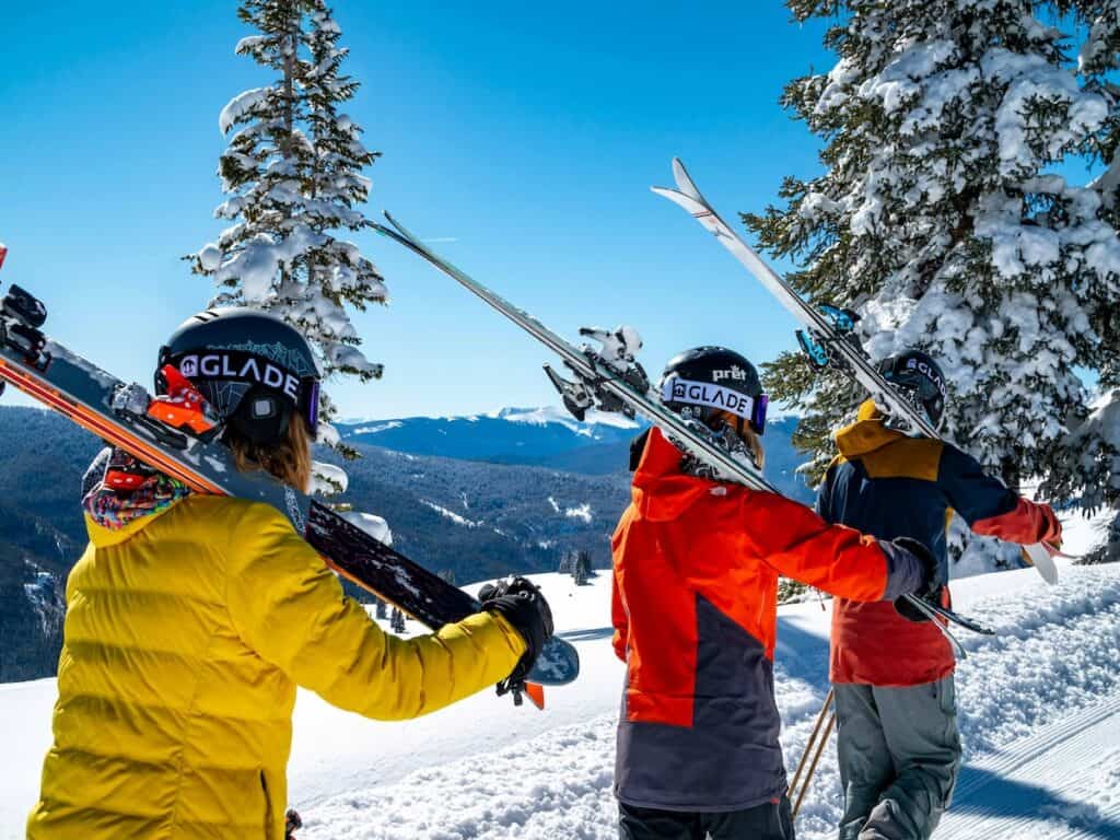 Three skiers holding their skis with blue skies above.