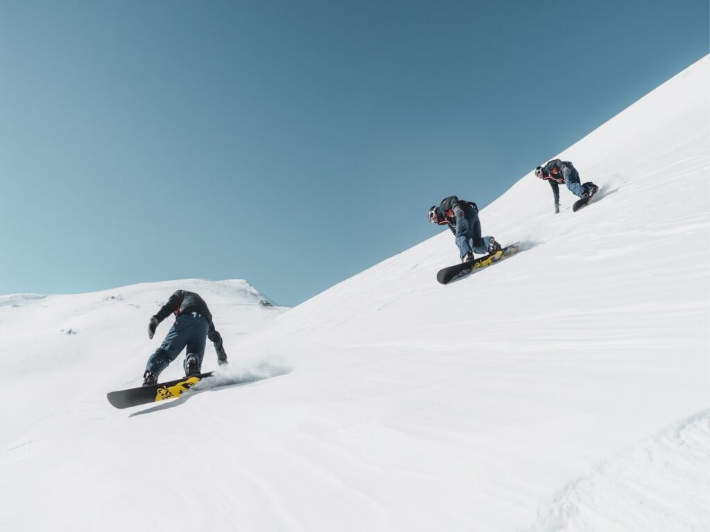 Three snowboarders following each other down the ski slope.