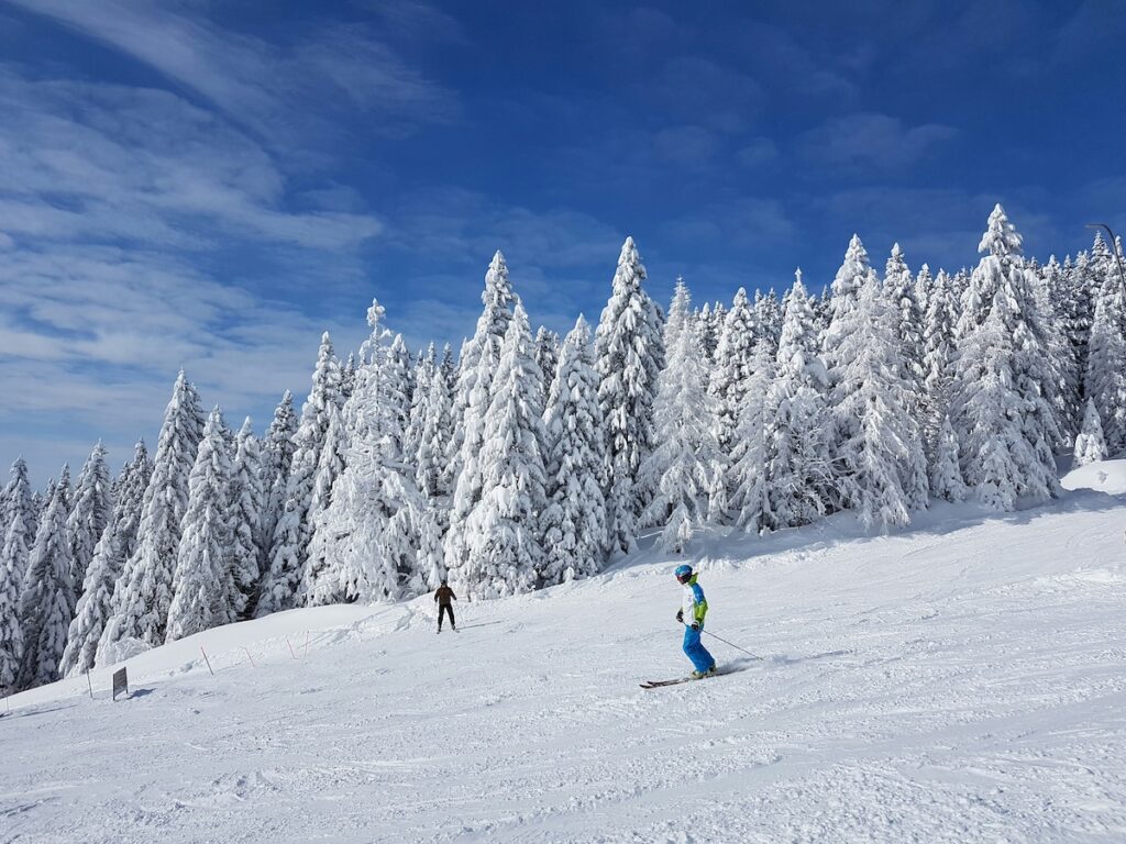 Two skiers going down the mountain with blue skies.