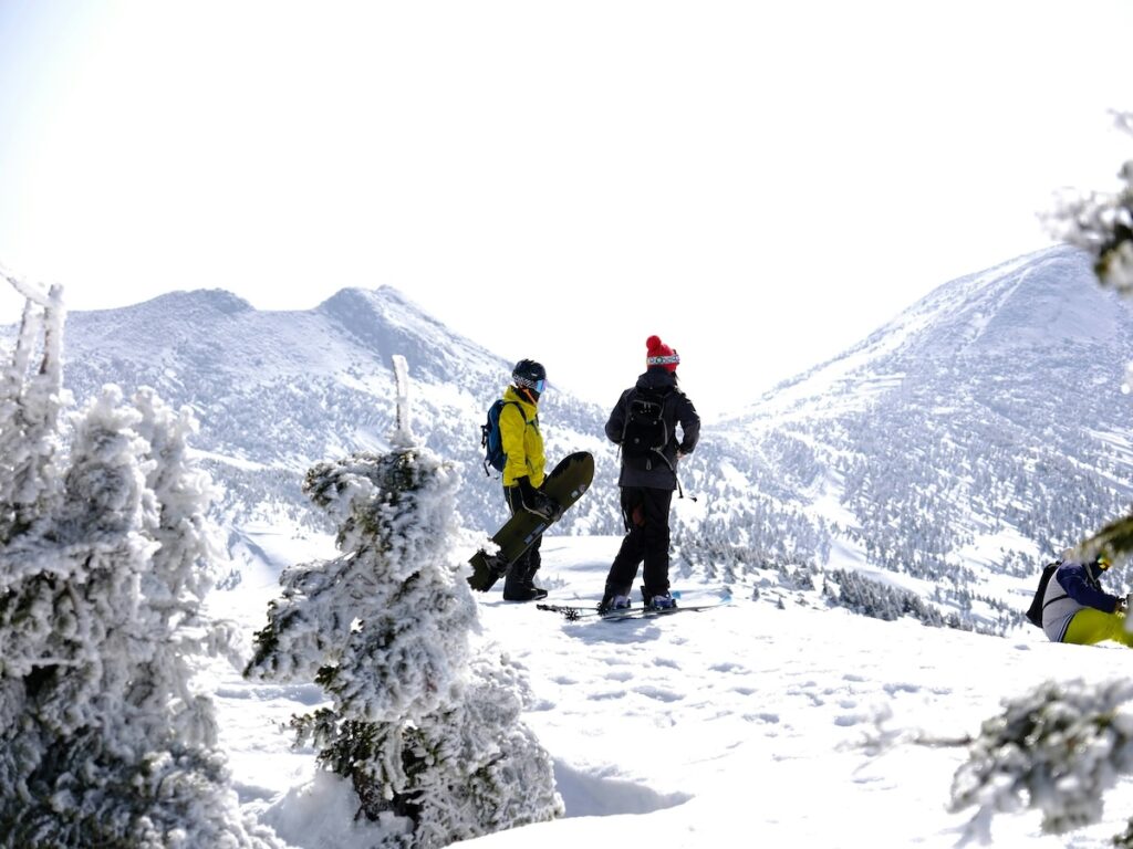 A snowboarder and a skier looking out at the mountains. 