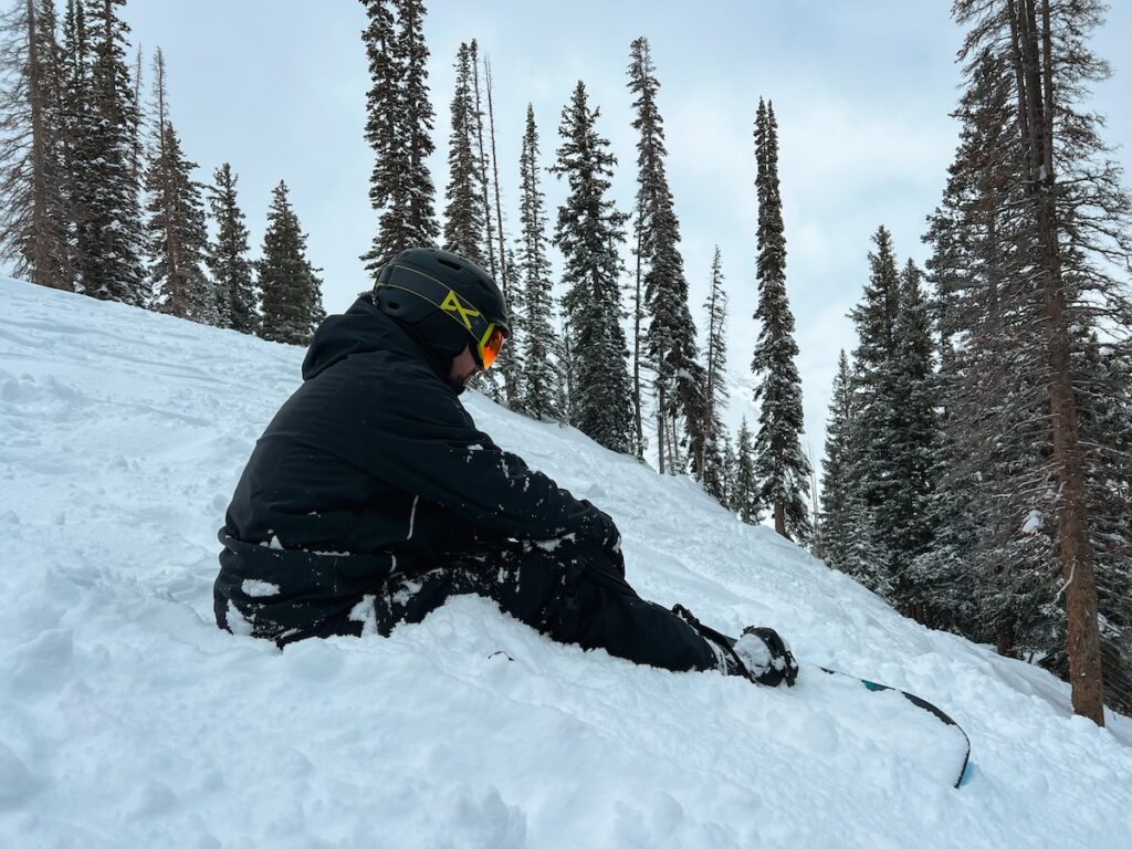 Sam sitting on the slopes wearing one of the best snowboard helmets with bluetooth. 