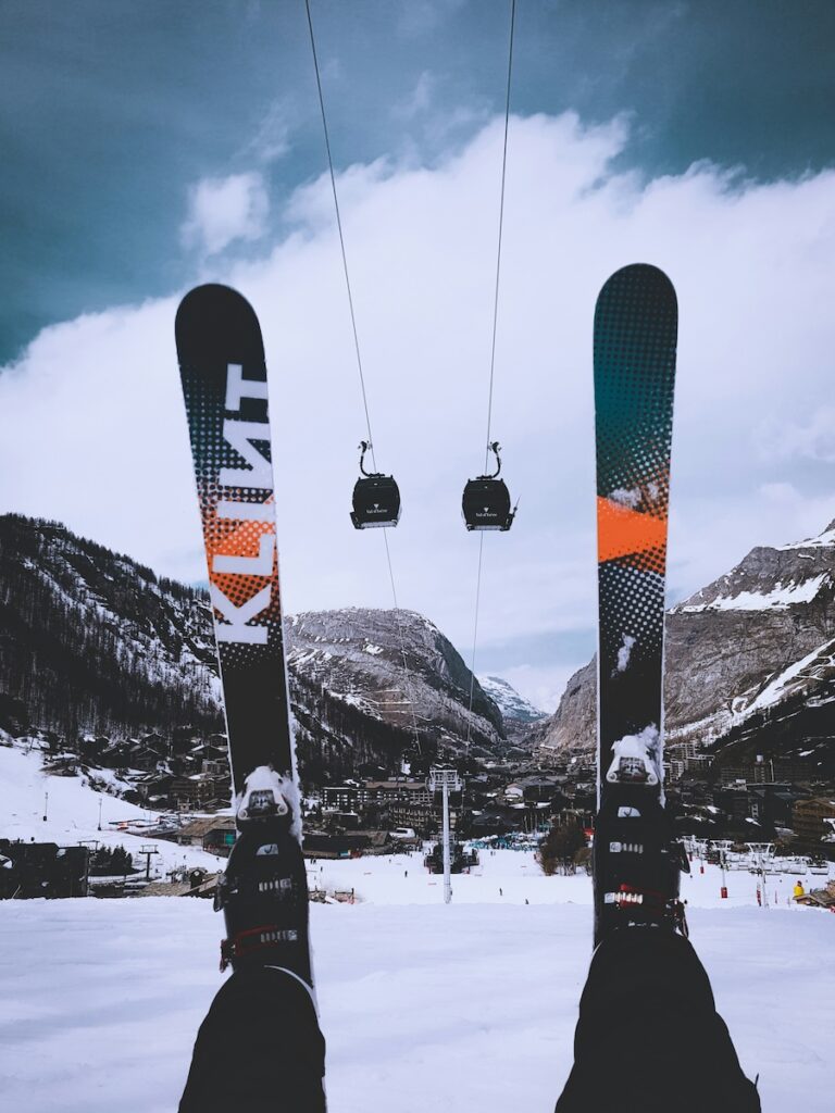 A pair of boots and skis pointing up with gondolas and mountains off in the distance.