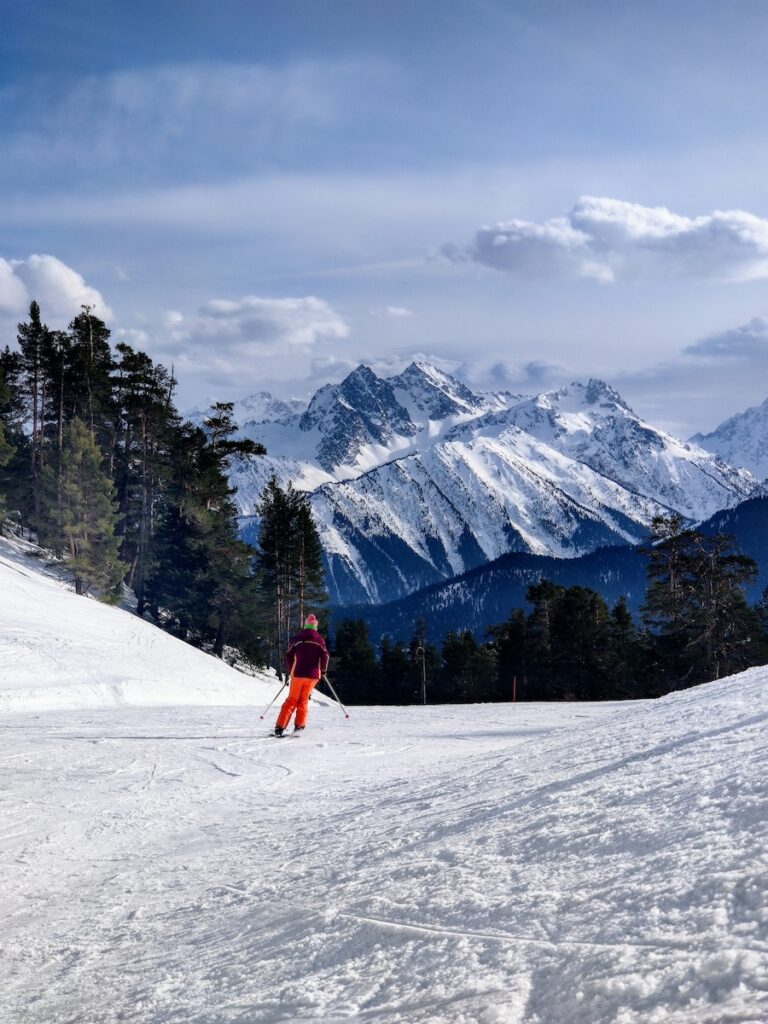 A skier going down an easy trail with mountains in the distance.