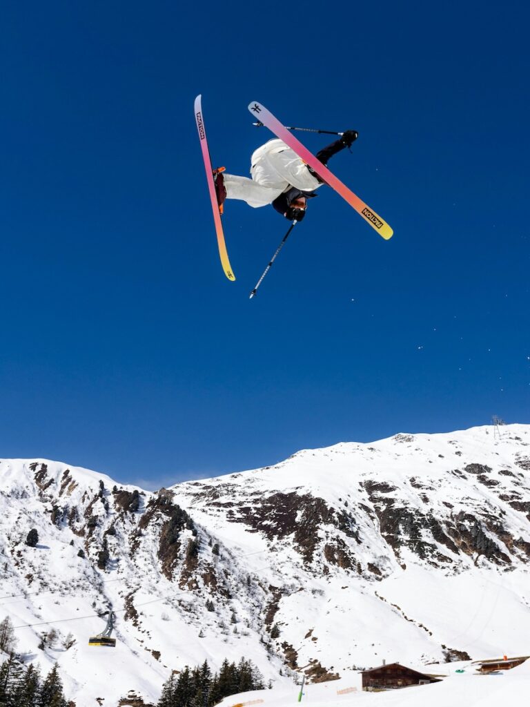 A skier jumping in the air with colorful skis on.