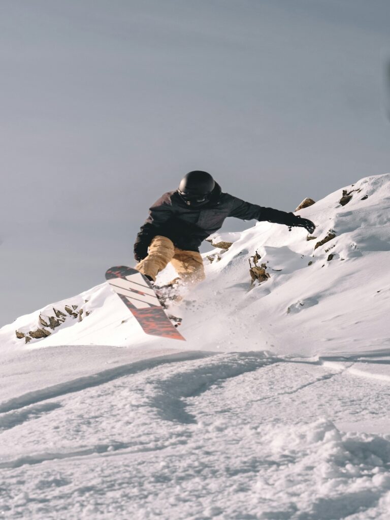 A snowboarder jumping in the air with rocks behind him.