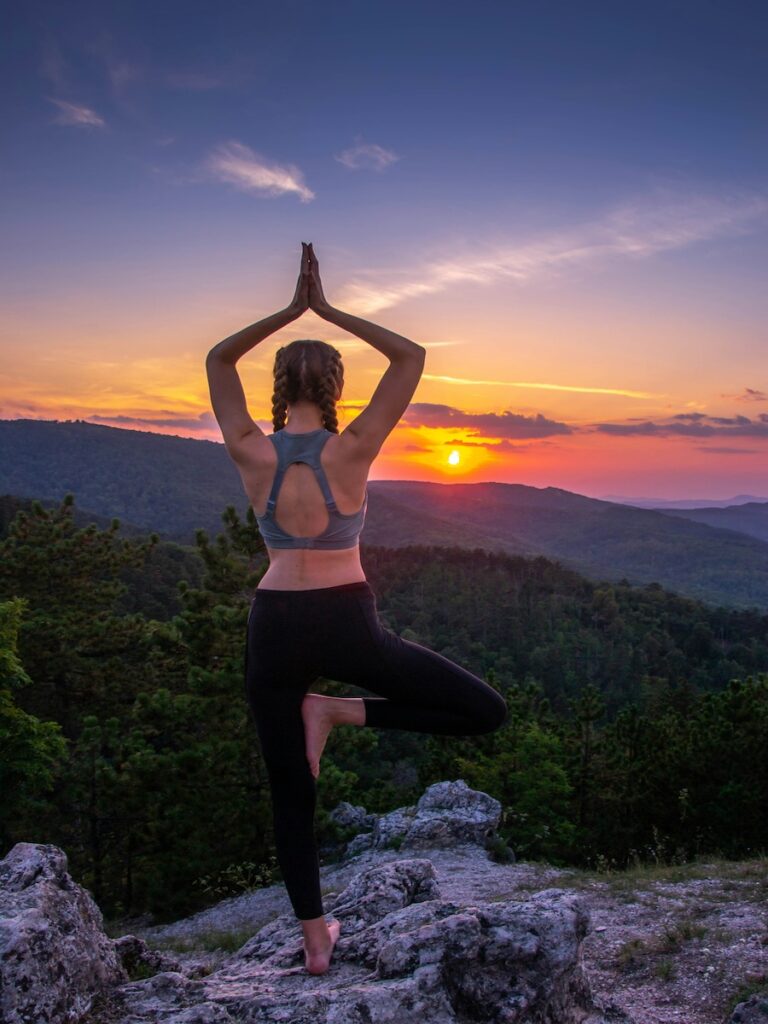 A woman balancing while doing yoga as the sun sets.