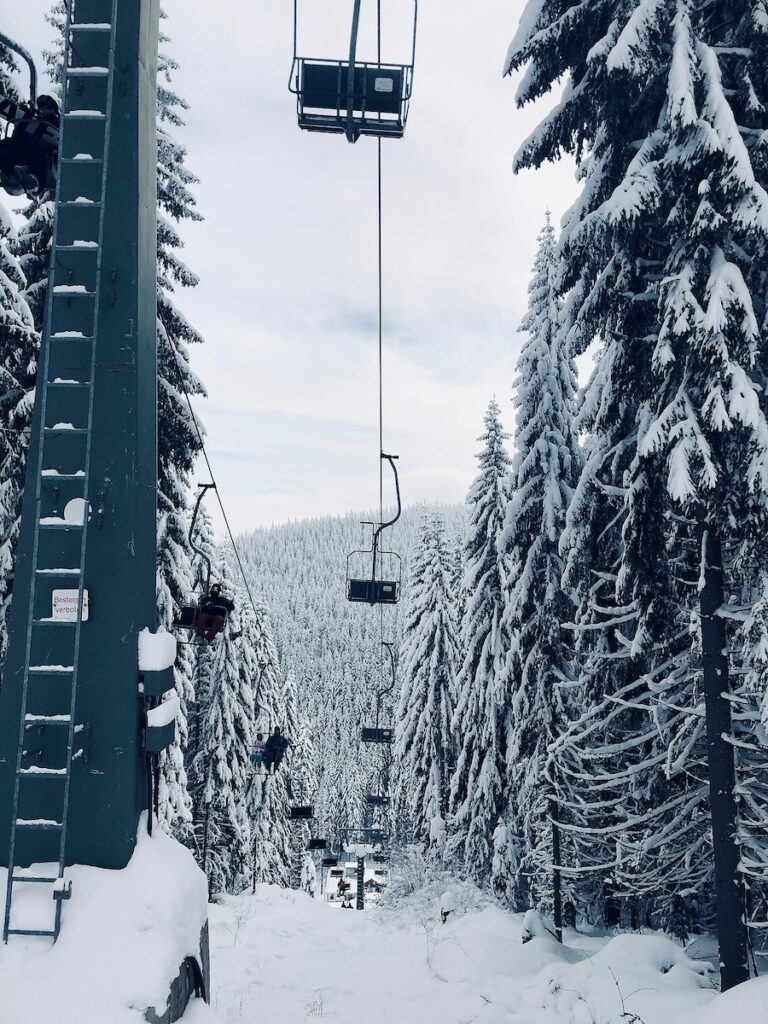 A chairlift in operation passing by snow covered trees.