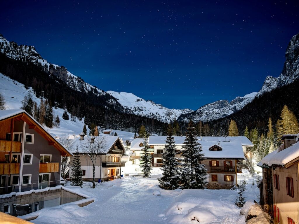 A ski village at night lit up by lights, surrounded by mountains, covered in snow.