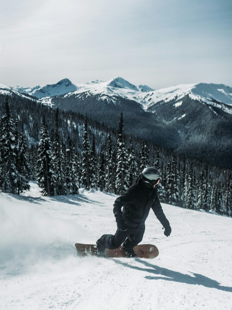 A snowboarder on his edge going down the ski slopes with mountains in the distance. 