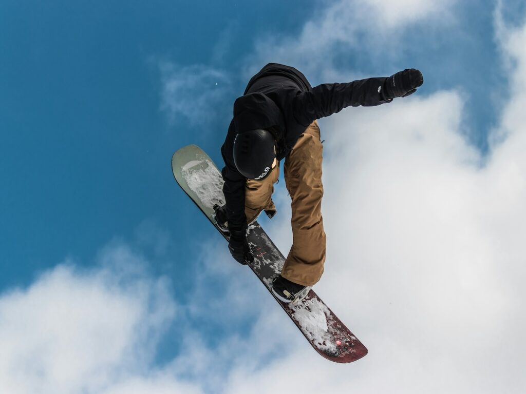 A snowboarder jumping high in the air with tan pants and a black jacket on.