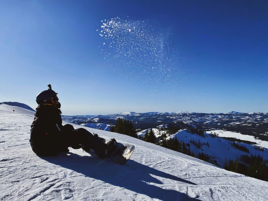 A snowboarder sitting on the mountain with blue skies.