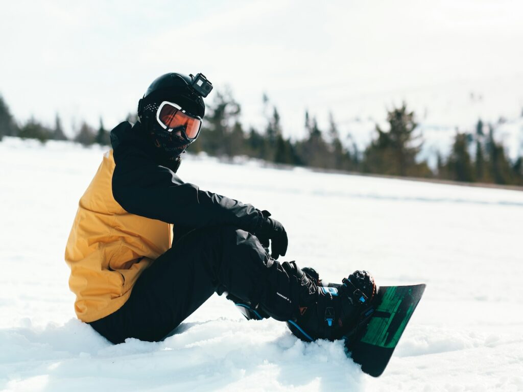 A snowboarder sitting in a yellow and black jacket on a ski slope.