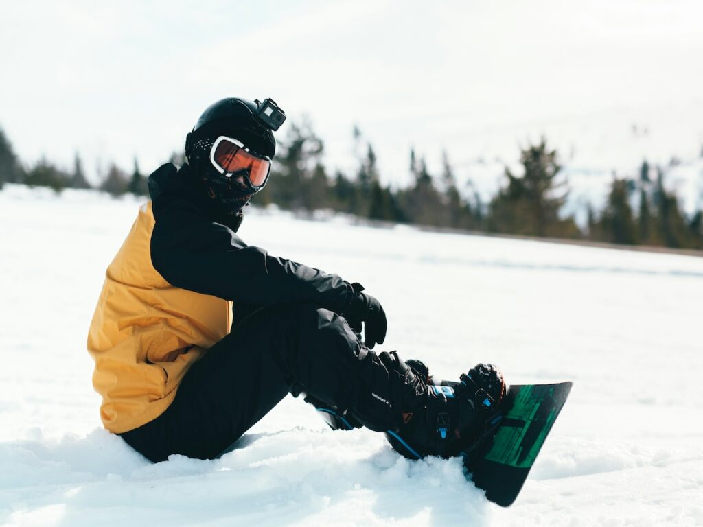 A snowboarder in a yellow and black jacket sitting down on the ski slope.