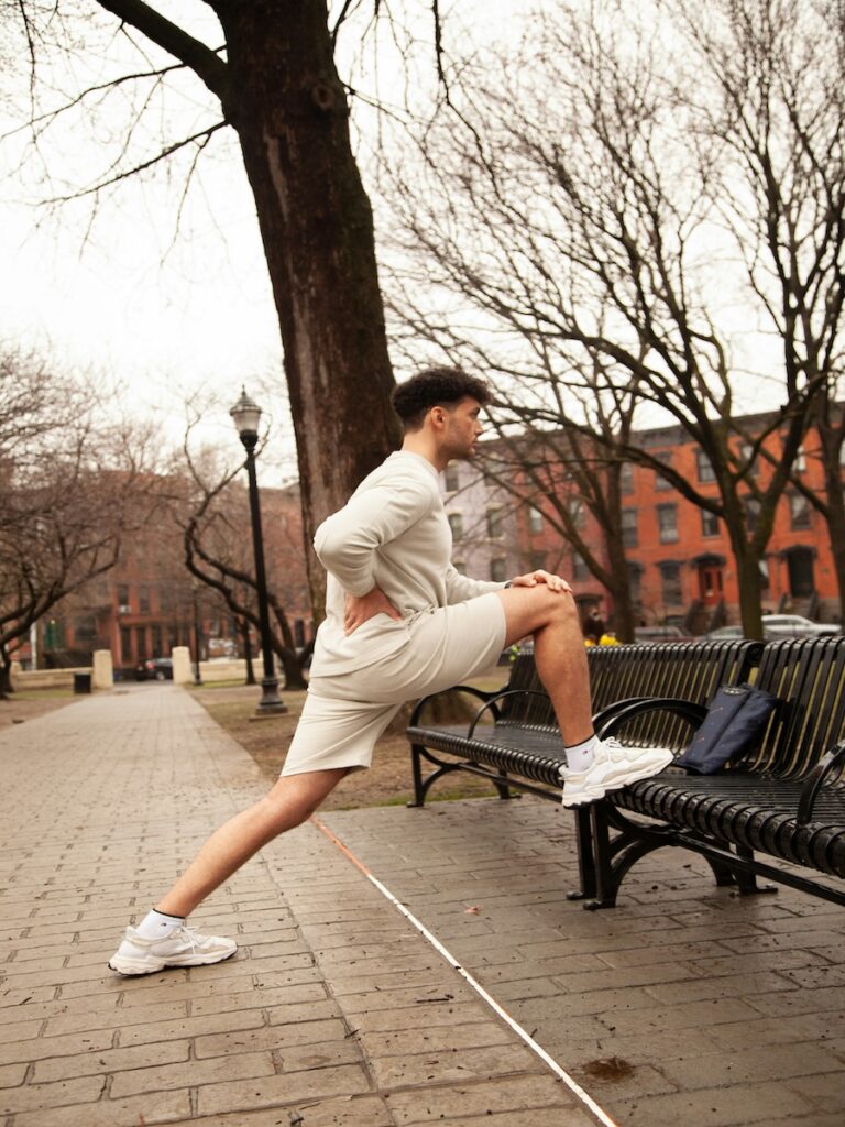 A man stretching his leg on a park bench.