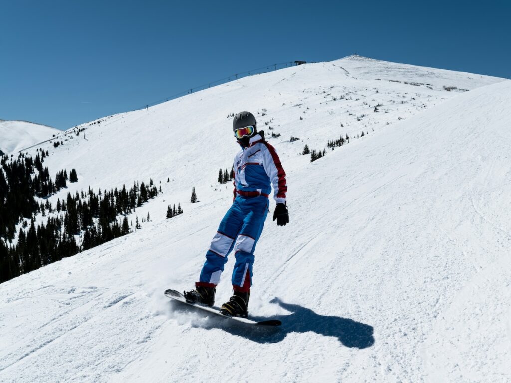 A snowboarder going gently down a ski slope with blue skies above.