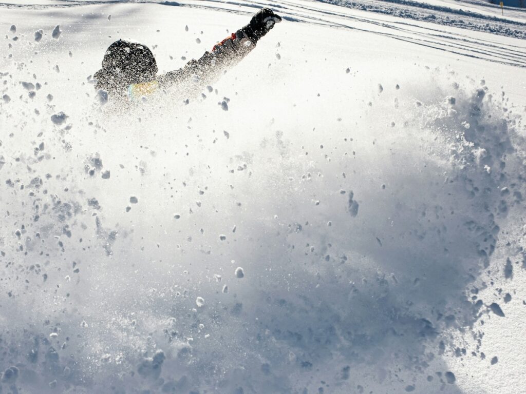 How to safely fall snowboarding as a snowboarder sprays up chunks of snow.