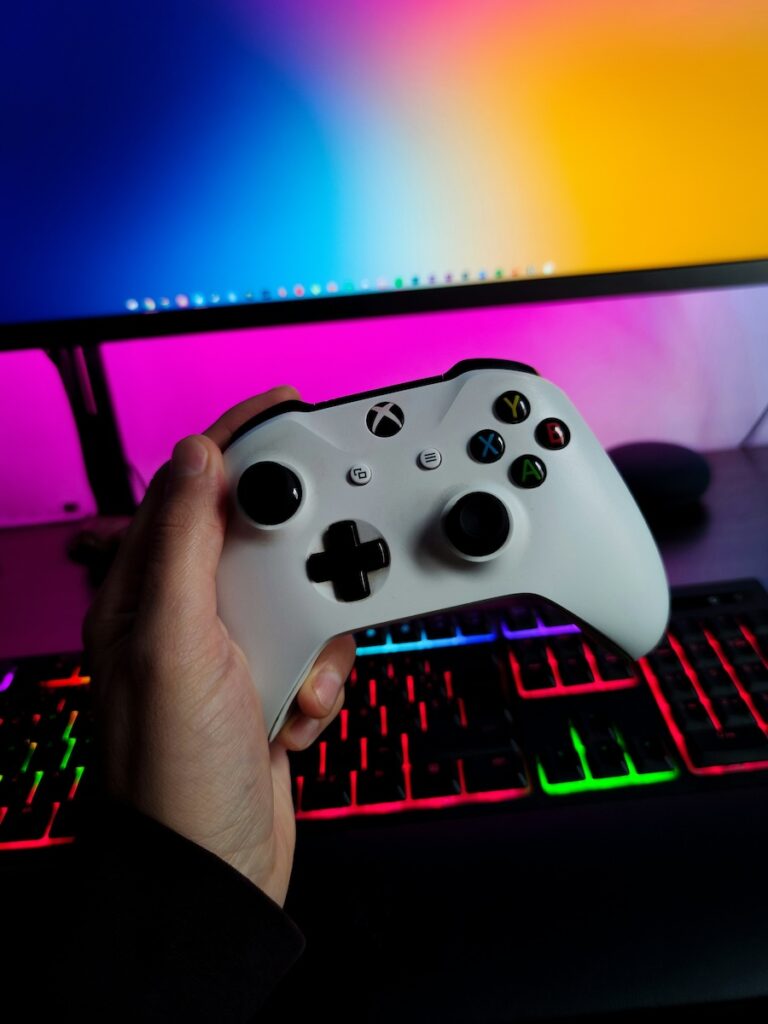 A video game controller and a computer in the background.