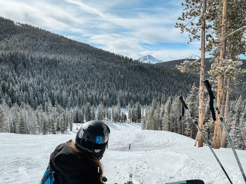 Abby sitting on the slopes in Breckenridge looking out at snow covered trees and mountains.