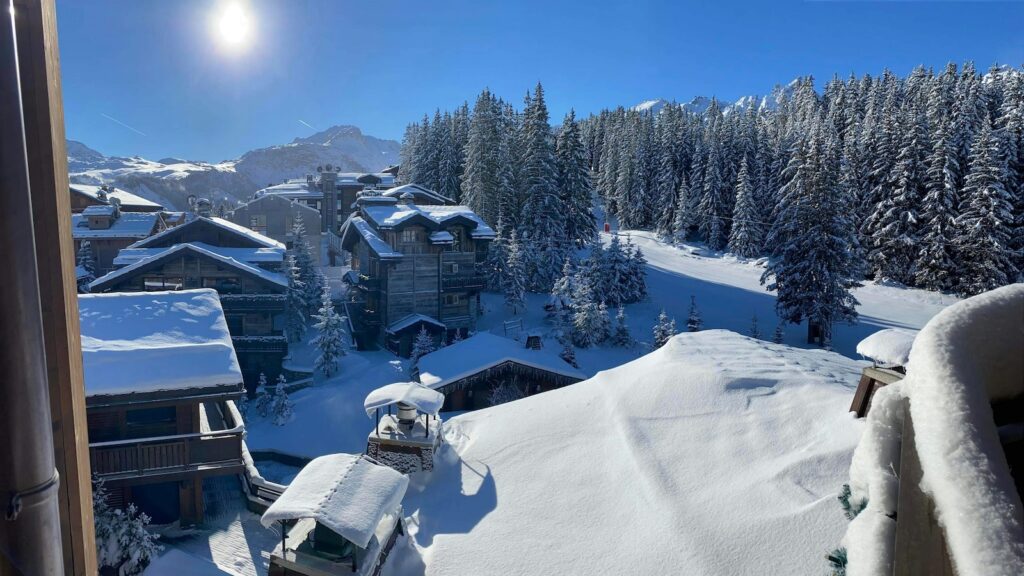 Snow covered buildings and trees with blue skies above at Courchevel in France.