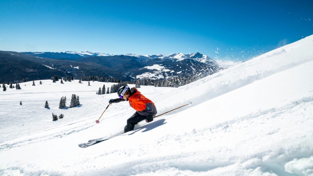 A skier going down the mountain on a bluebird day in a red jacket.