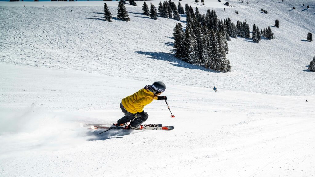 A skier going down the slopes in a bright yellow jacket.