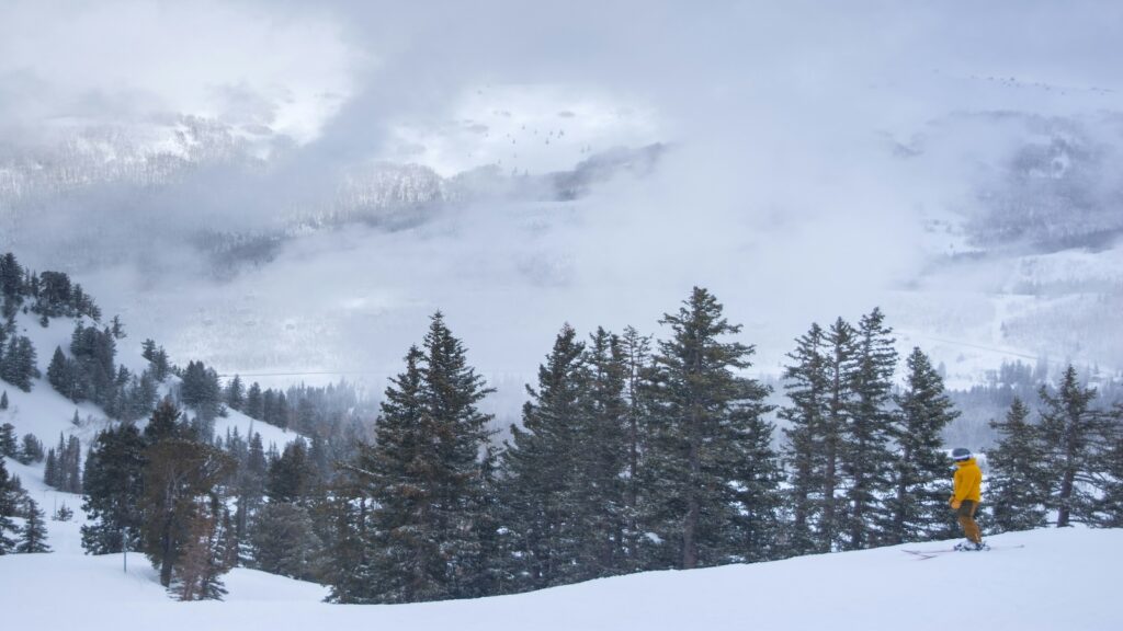 A skier in a yellow jacket looking down the ski resort in Utah.