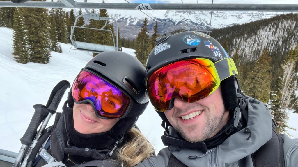 Abby and Sam smiling on a chairlift at a ski resort.