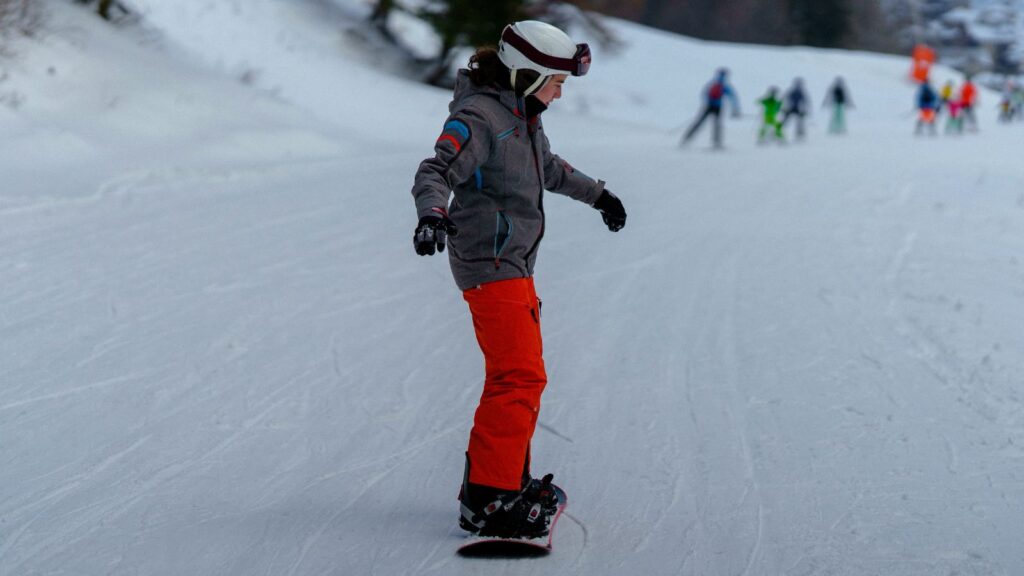 A beginner snowboarder in red pants and a grey jacket.