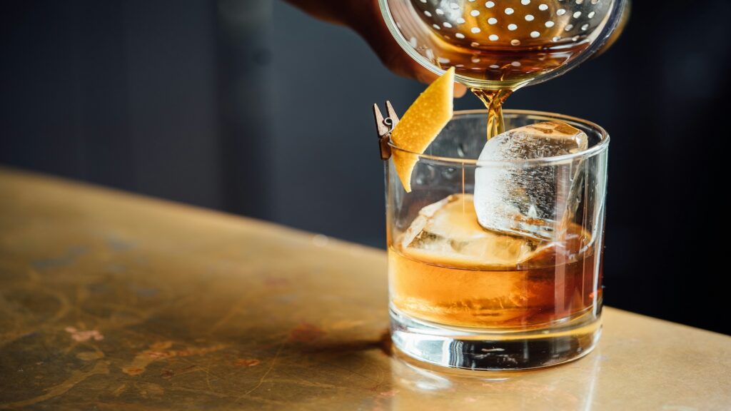 A bourbon cocktail being poured.