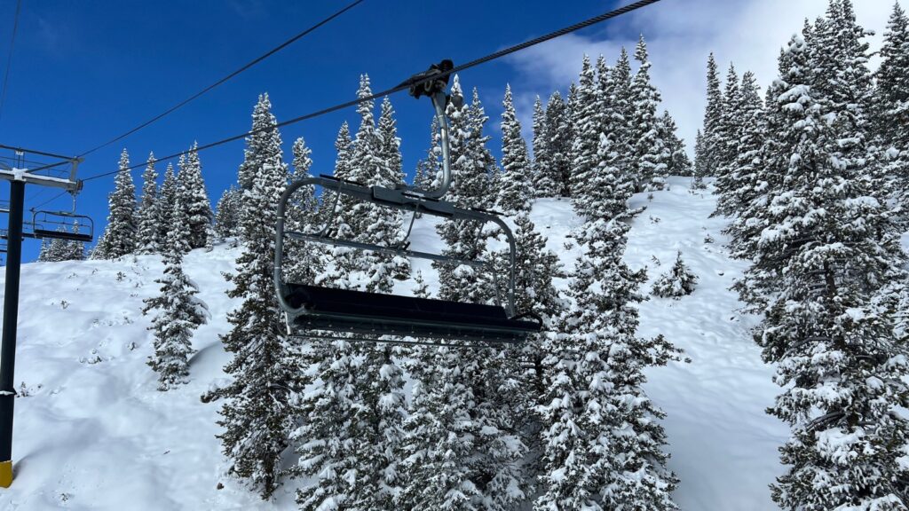 An empty chairlift going down the mountain with snow covered trees behind.