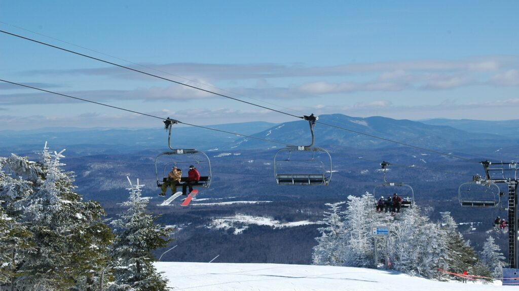 Snowboarders riding a chairlift at Okemo Mountain.