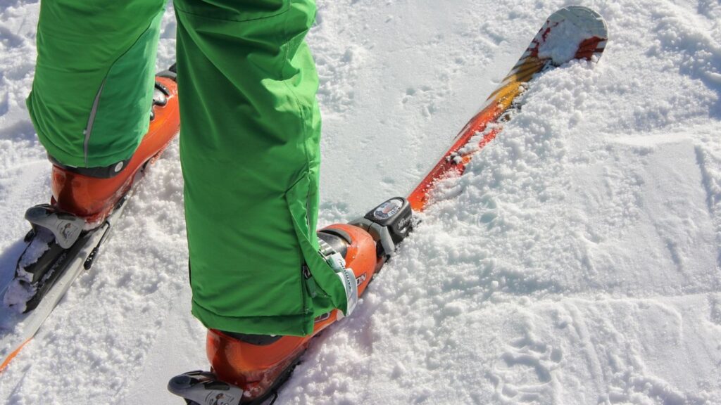 A skier with green pants and orange skis on.