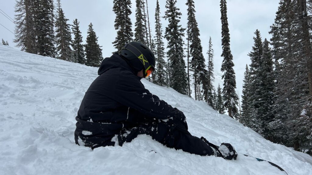 Sam sitting in snow while strapped into his board at a ski resort.