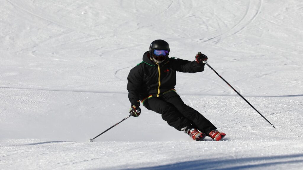 A skier going fast down a groomed run in all black.