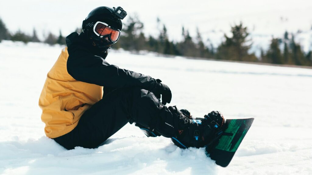 A snowboarder sitting with a yellow and black jacket on.