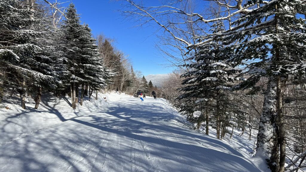 Snowboarders going down a groomed run in Vermont on a bluebird day.