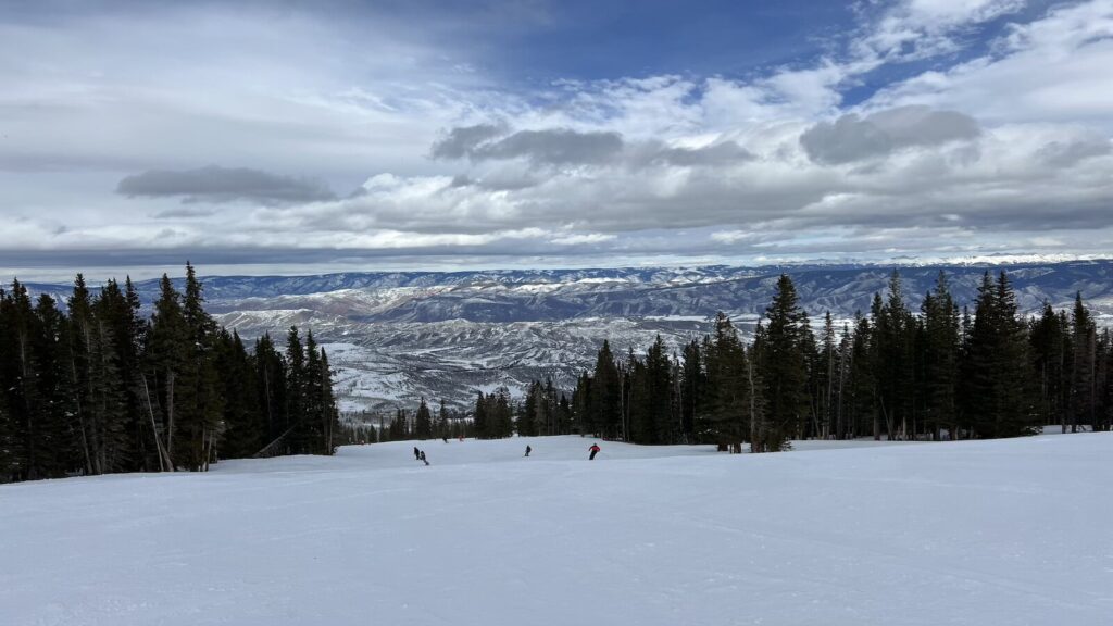 A groomed run at Aspen Snowmass surrounded by trees.